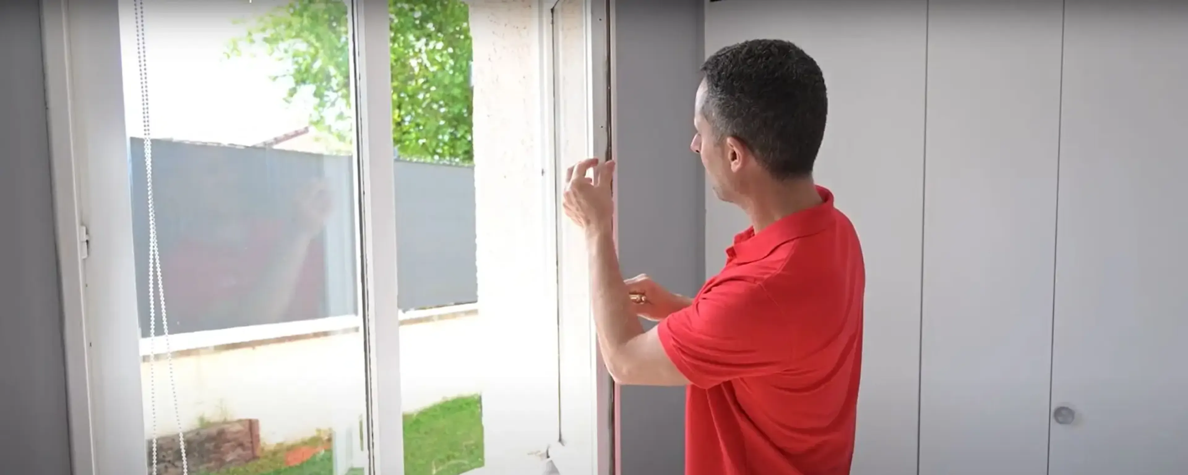 Homme en rouge inspectant le joint d'une fenêtre en PVC