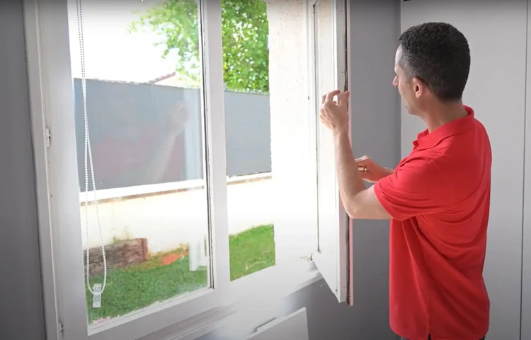 Homme en rouge inspectant le joint d'une fenêtre en PVC