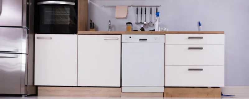 Fuite d'eau sur carrelage blanc devant un lave-vaisselle dans une cuisine