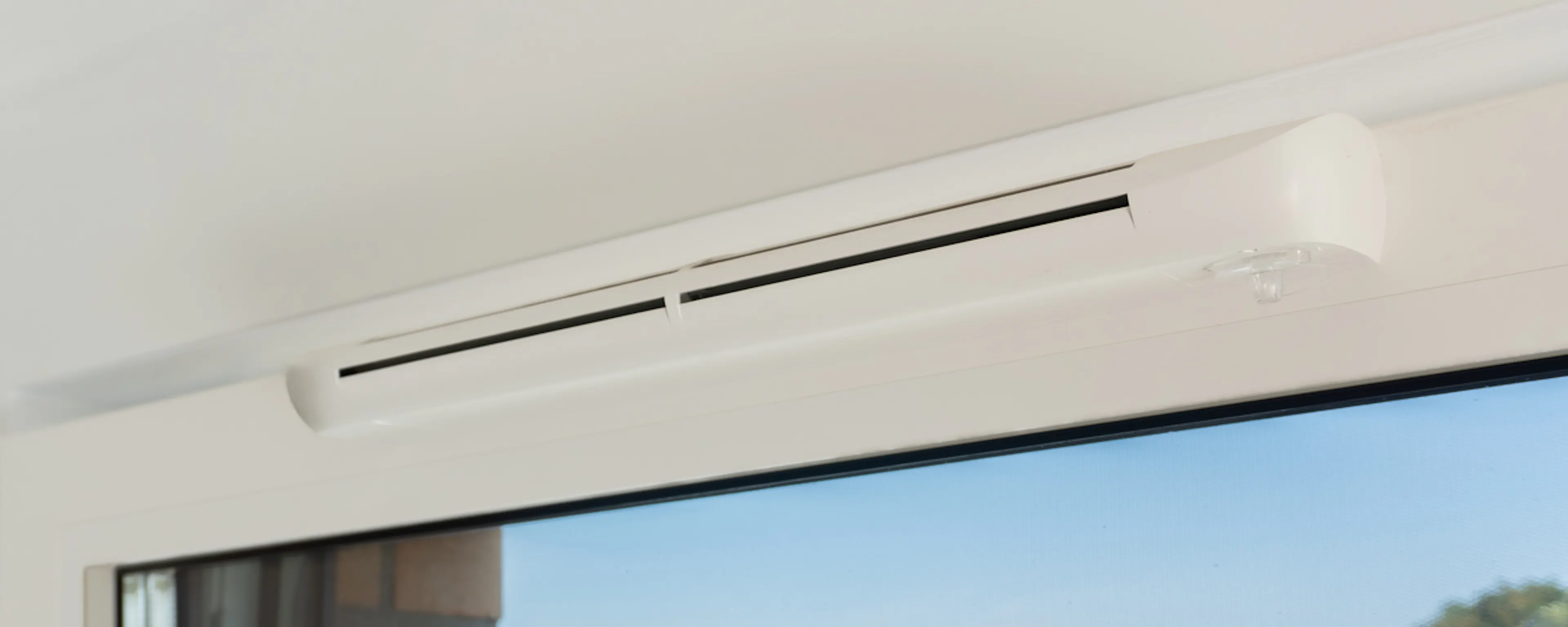 Gros plan sur une grille d'aération de fenêtre installée sur une menuiserie PVC blanche