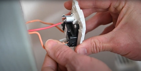 Mains connectant des fils électriques orange sur un interrupteur mural