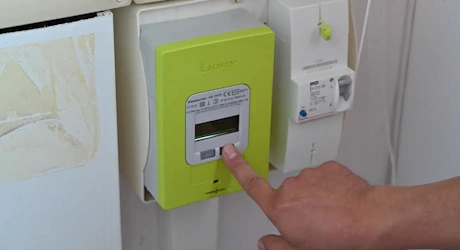 Main appuyant sur le bouton d'un compteur électrique Linky vert