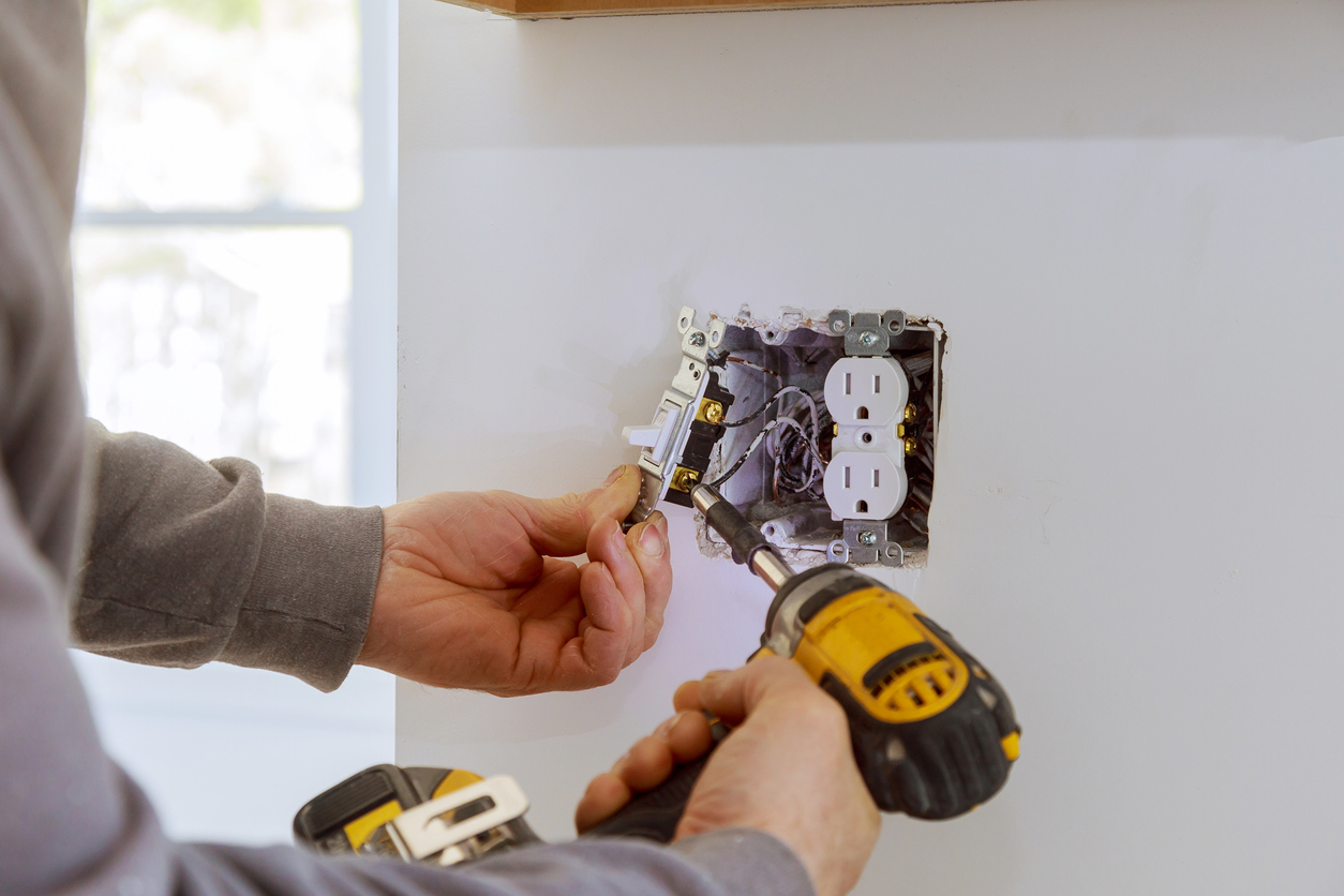 Électricien installant une prise murale avec une perceuse jaune