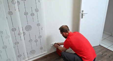 Homme accroupi réparant une prise électrique murale dans un couloir