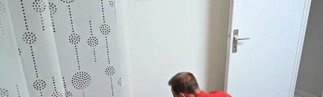 Homme accroupi réparant une prise électrique murale dans un couloir