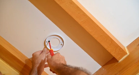Mains vissant un détecteur de fumée au plafond à l'aide d'un tournevis
