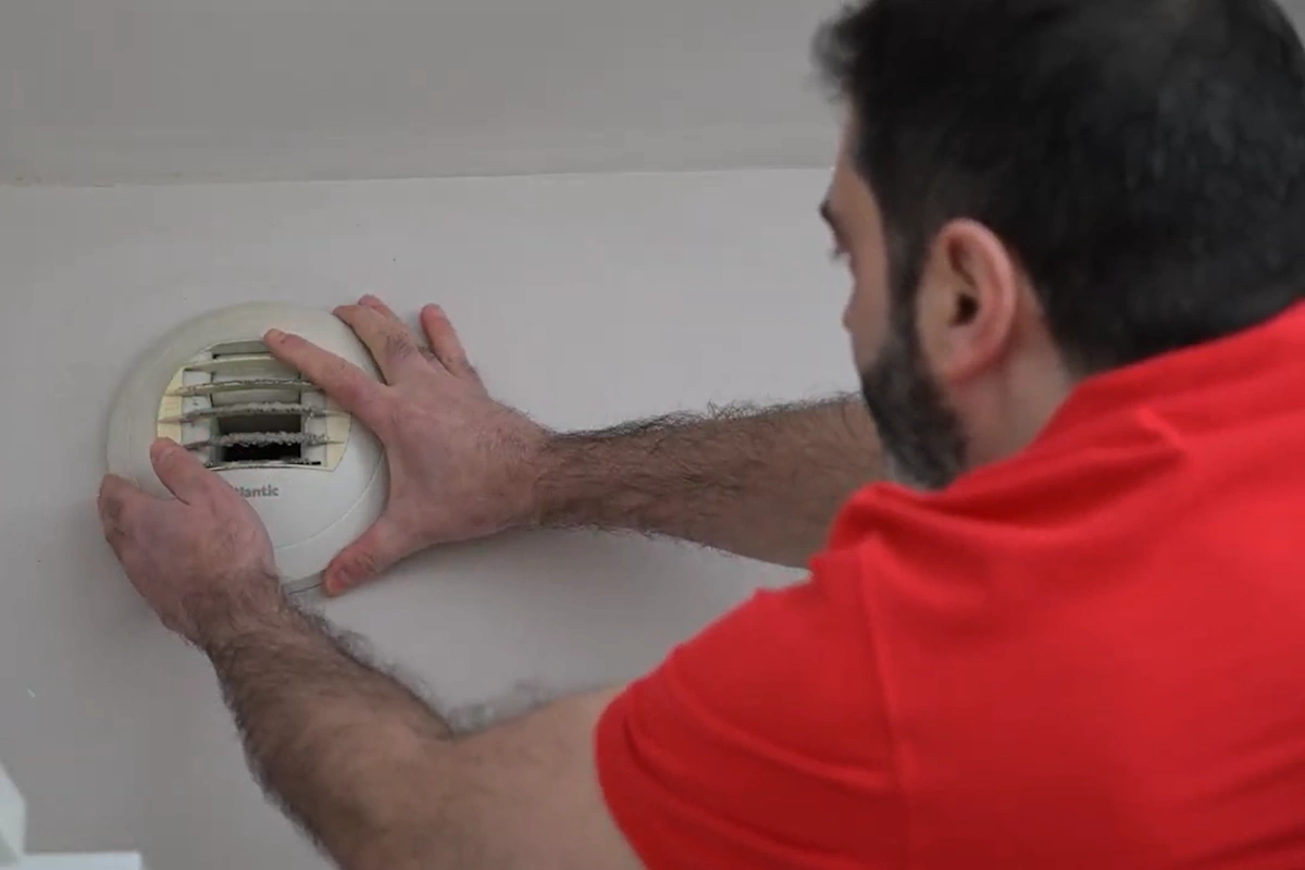 Technicien en polo rouge installant un détecteur de fumée au plafond