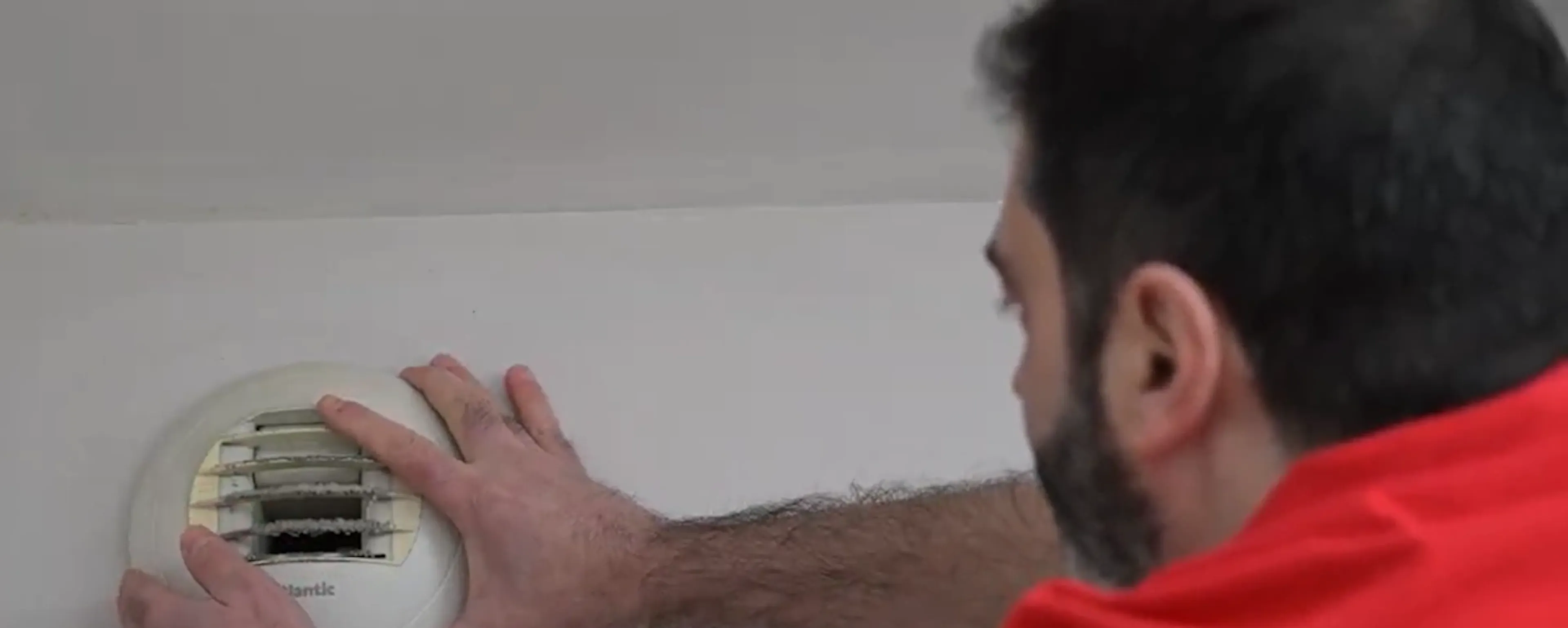 Technicien en polo rouge installant un détecteur de fumée au plafond