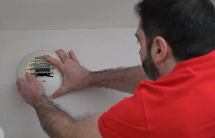 Technicien en polo rouge installant un détecteur de fumée au plafond