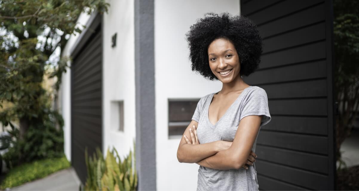 Femme souriante aux bras croisés devant une maison moderne