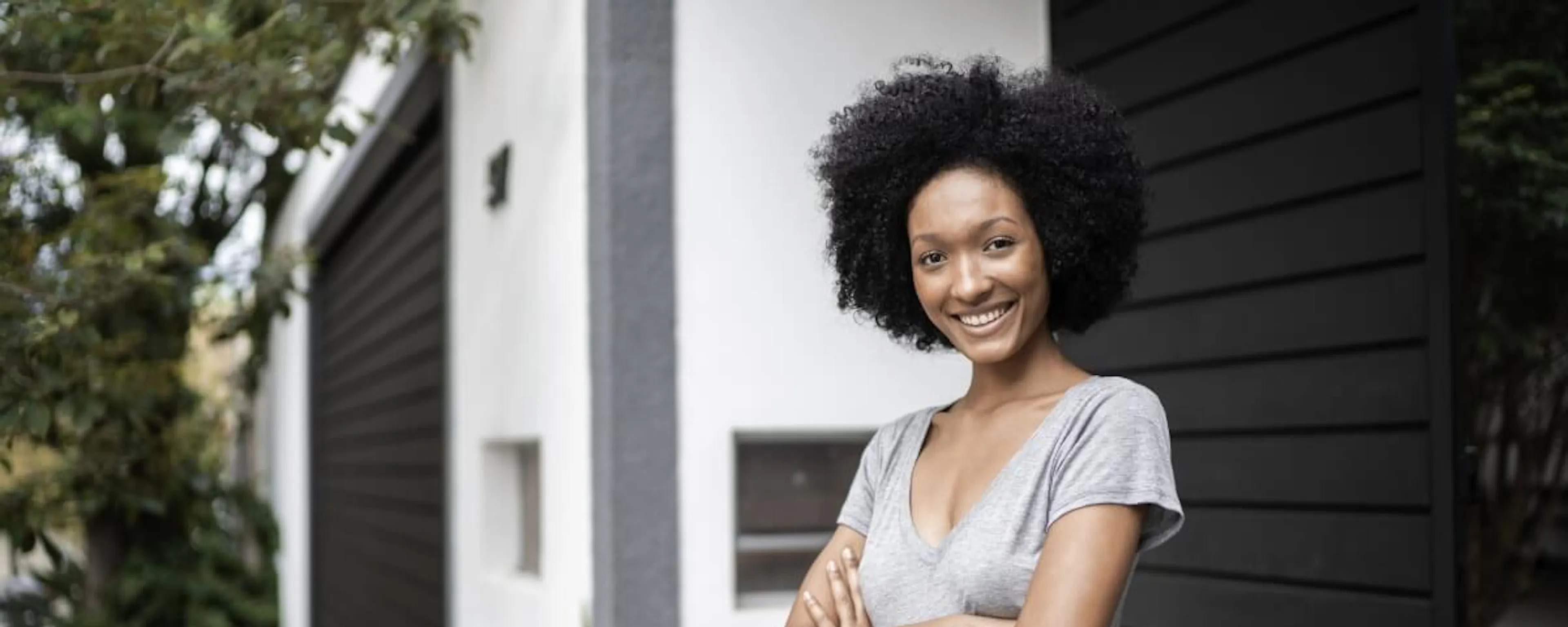 Femme souriante aux bras croisés devant une maison moderne
