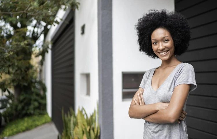Femme souriante aux bras croisés devant une maison moderne
