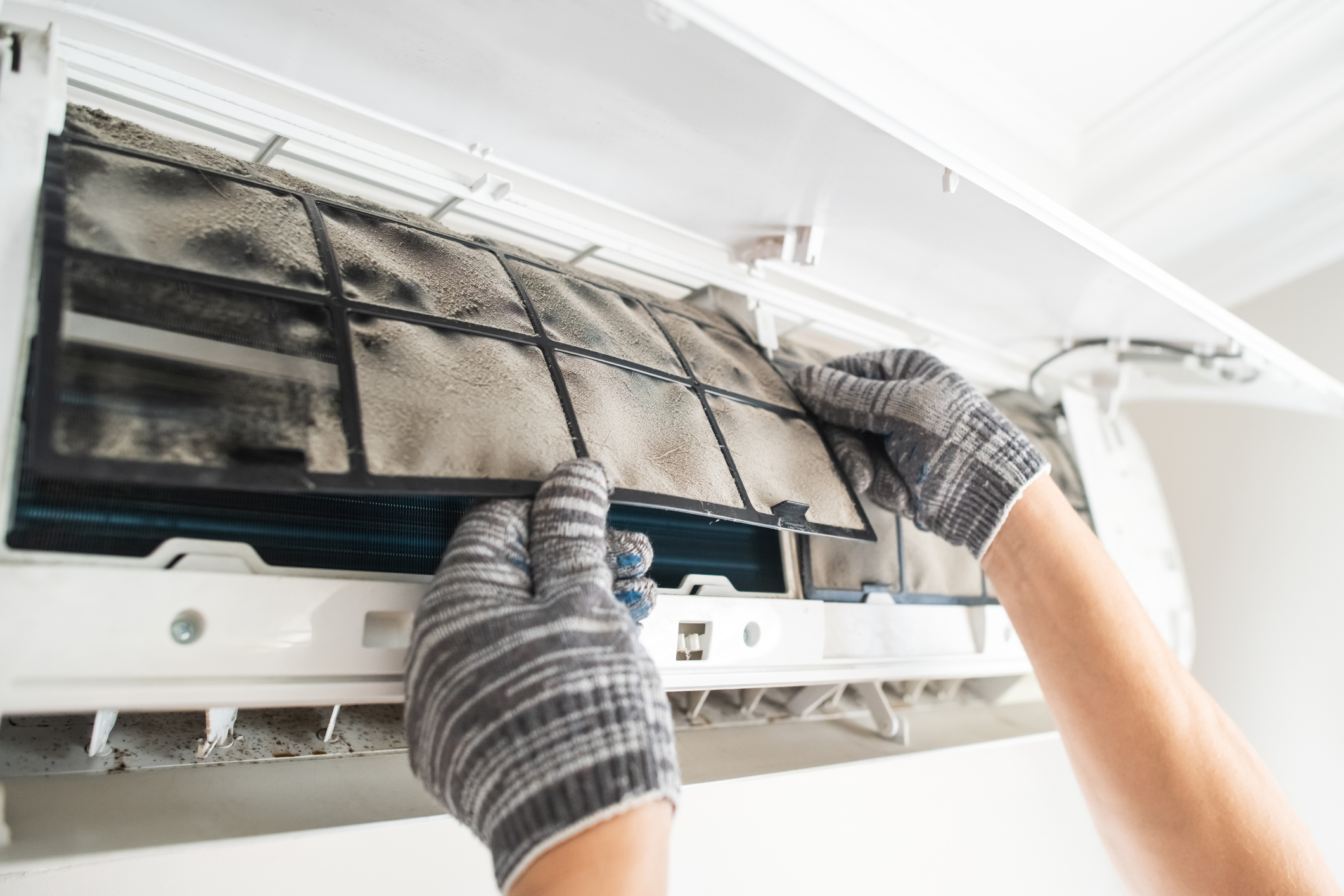 Un particulier retire délicatement le filtre à poussière de son climatiseur split pour l'entretenir