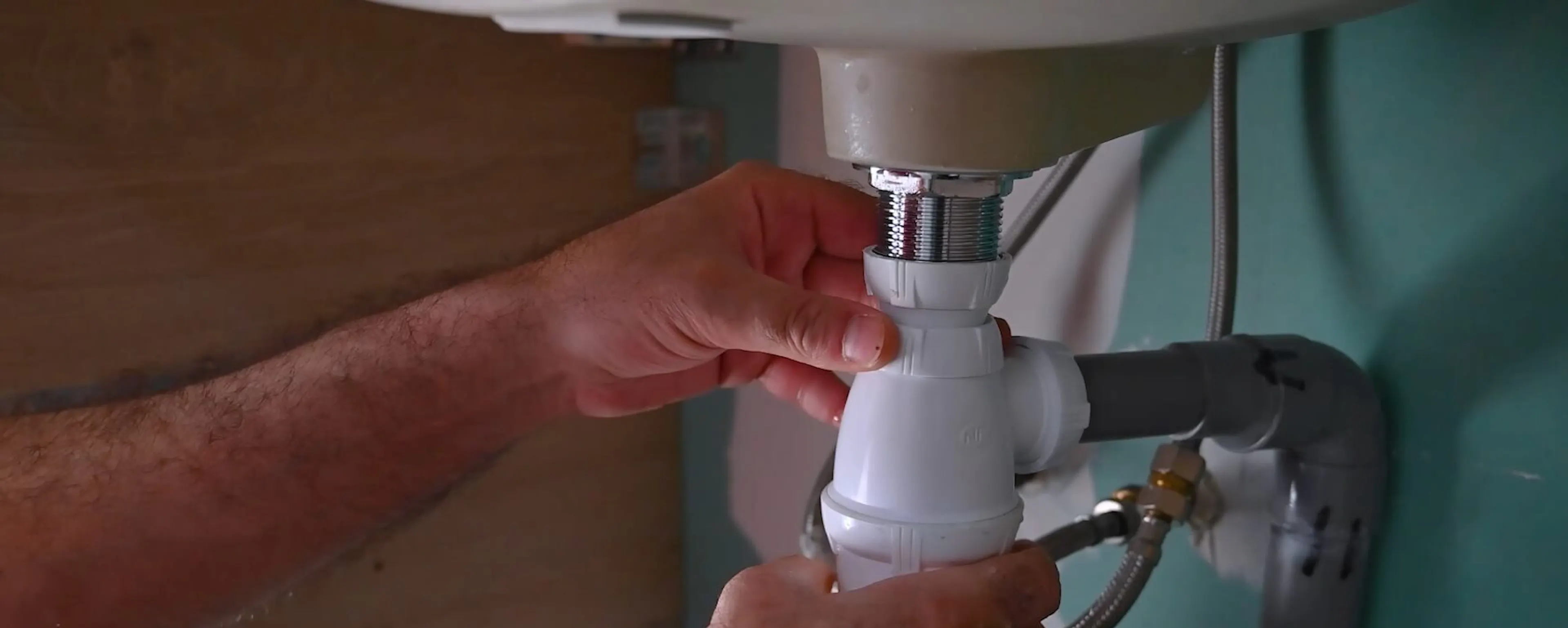 Mains resserrant le siphon en PVC sous un lavabo
