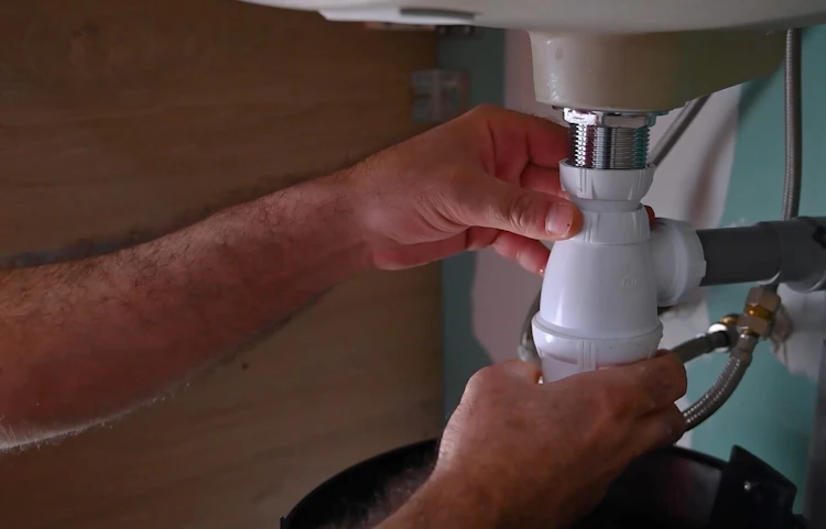 Mains resserrant le siphon en PVC sous un lavabo