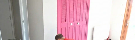 Technicien en rouge accroupi devant un radiateur rose dans une pièce carrelée