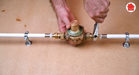 Mains serrant un réducteur de pression sur une canalisation en cuivre