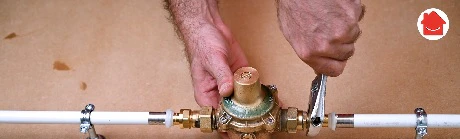 Mains serrant un réducteur de pression sur une canalisation en cuivre
