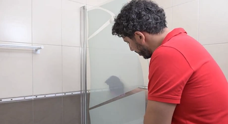 Homme inspectant une paroi de douche en verre dans une salle de bain
