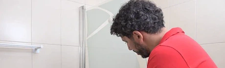Homme inspectant une paroi de douche en verre dans une salle de bain
