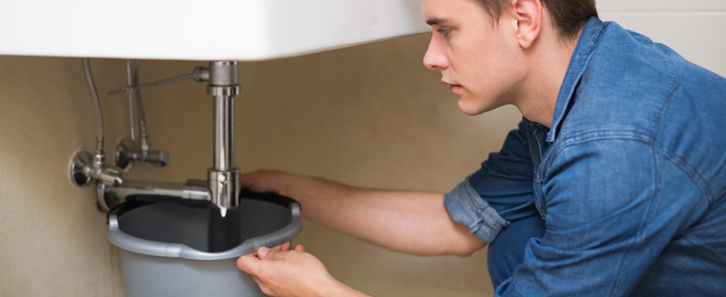 Jeune homme réparant la plomberie sous un lavabo de salle de bain