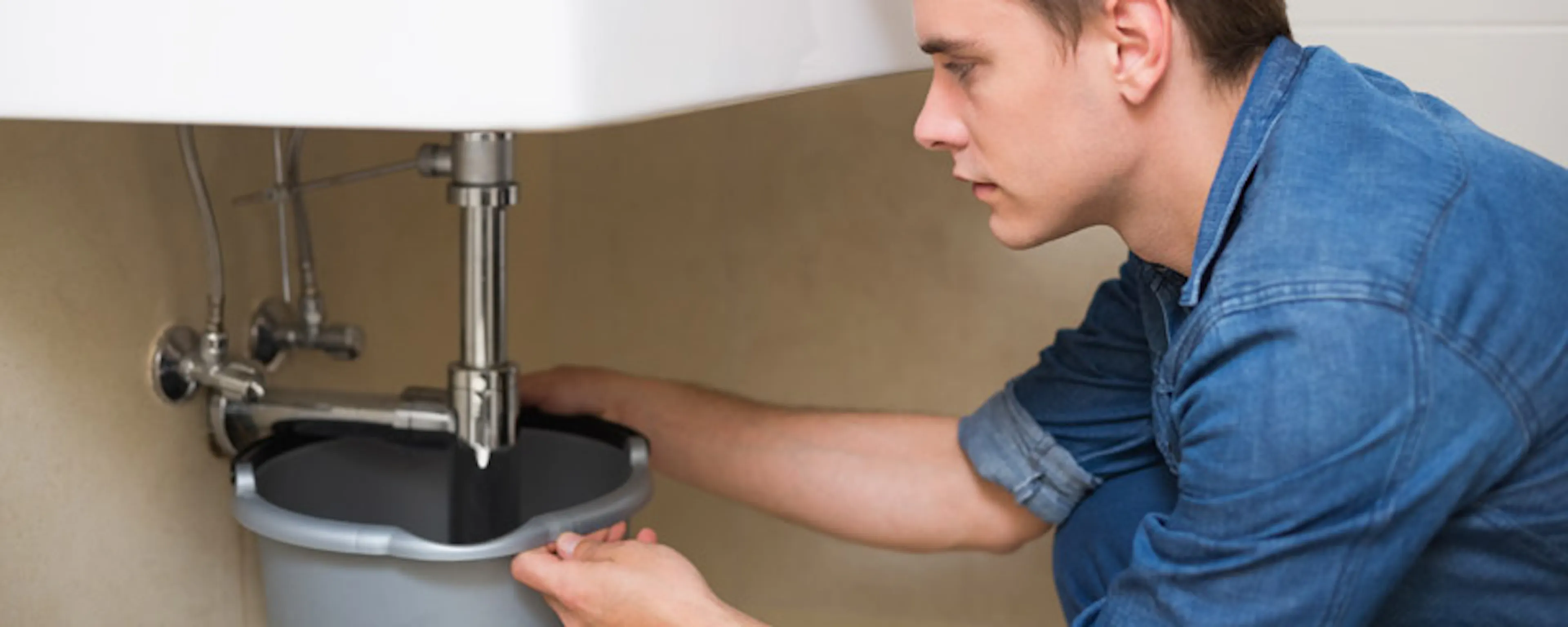 Jeune homme réparant la plomberie sous un lavabo de salle de bain
