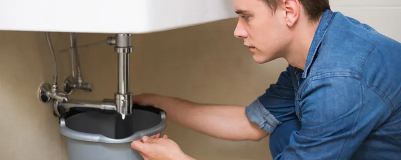 Jeune homme réparant la plomberie sous un lavabo de salle de bain