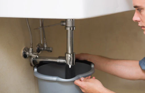 Jeune homme réparant la plomberie sous un lavabo de salle de bain