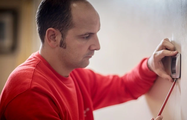 Homme en rouge installant ou vérifiant un interrupteur mural