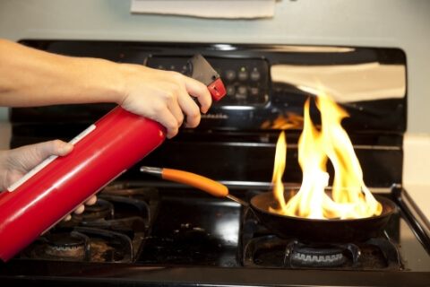 Main utilisant un extincteur rouge sur une poêle en feu