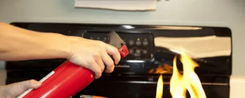 Main utilisant un extincteur rouge sur une poêle en feu