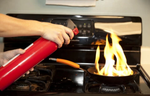 Main utilisant un extincteur rouge sur une poêle en feu