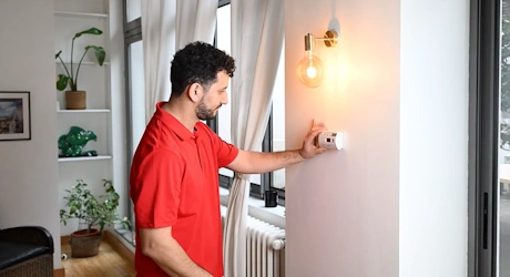 Technicien en rouge réglant un thermostat mural dans un appartement