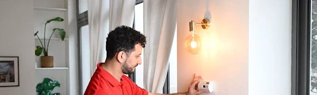 Technicien en rouge réglant un thermostat mural dans un appartement