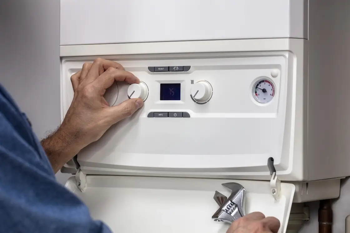 Main réglant les commandes d'une chaudière murale blanche