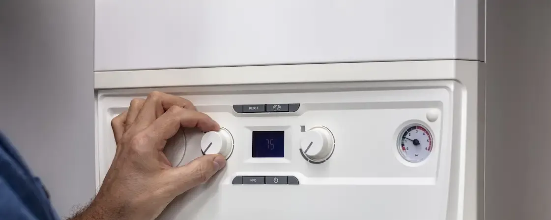 Main réglant les commandes d'une chaudière murale blanche