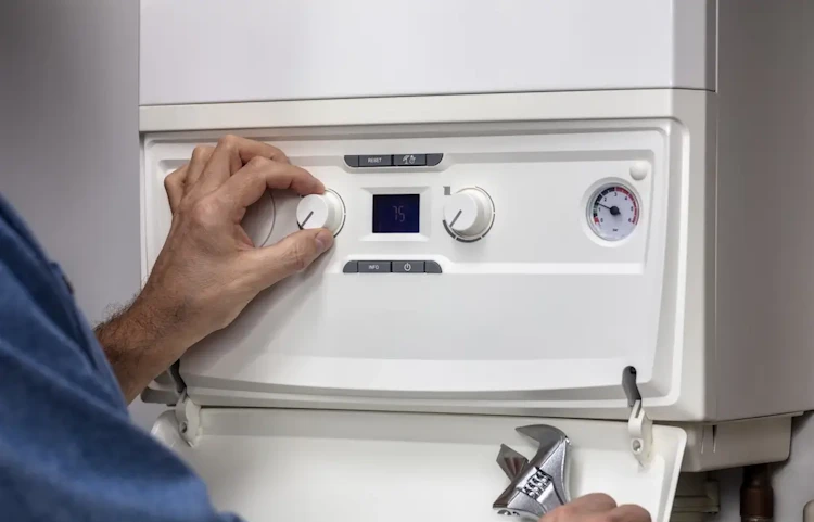 Main réglant les commandes d'une chaudière murale blanche