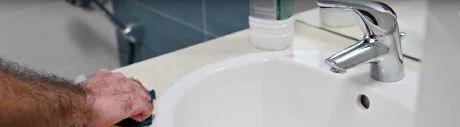 Main lissant le joint silicone neuf autour d'un lavabo avec une éponge
