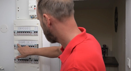 Technicien en rouge manipulant un disjoncteur dans un tableau électrique