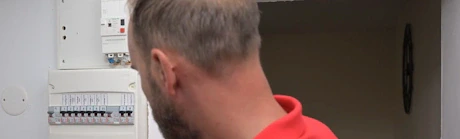 Technicien en rouge manipulant un disjoncteur dans un tableau électrique