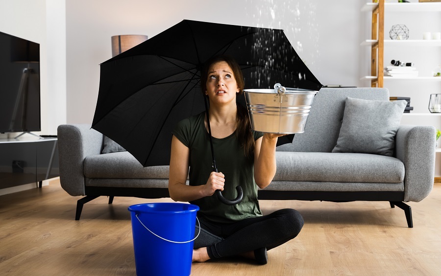 Femme assise sous parapluie avec seau récupérant une fuite de toit