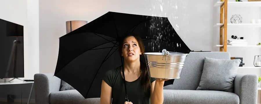 Femme assise sous parapluie avec seau récupérant une fuite de toit