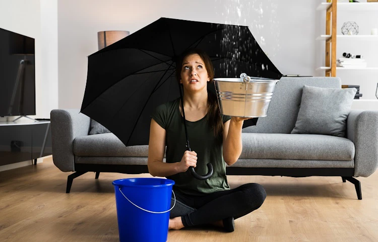 Femme assise sous parapluie avec seau récupérant une fuite de toit