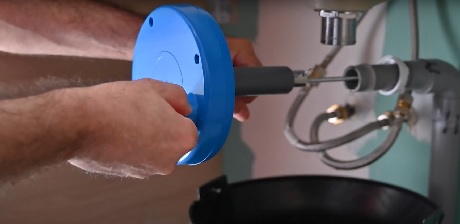 Mains installant un mécanisme de chasse d'eau bleu sur des tuyaux