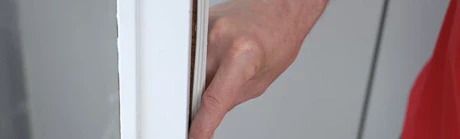 Main testant le joint d'étanchéité d'un bord de fenêtre blanche