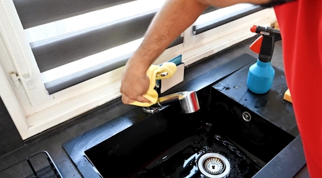 Technicien nettoyant un robinet d'évier noir avec une brosse