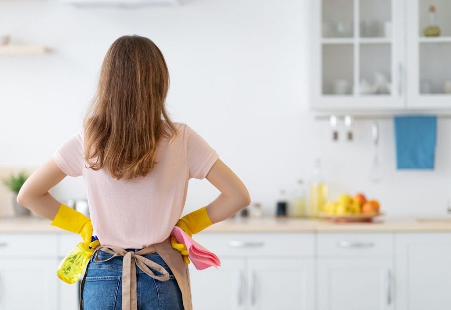 Femme de dos avec tablier et gants jaunes dans une cuisine blanche