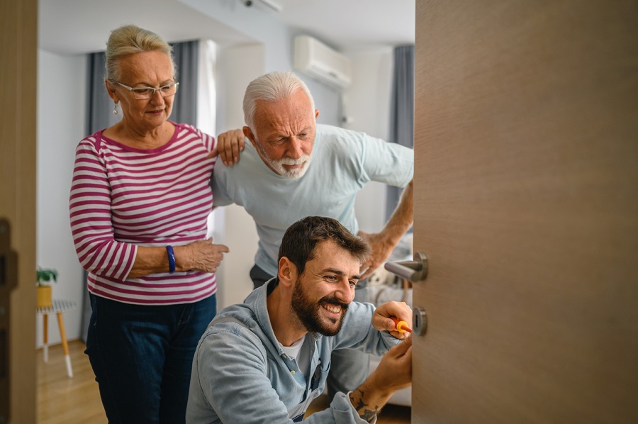 Technicien souriant réparant une porte chez un couple de seniors