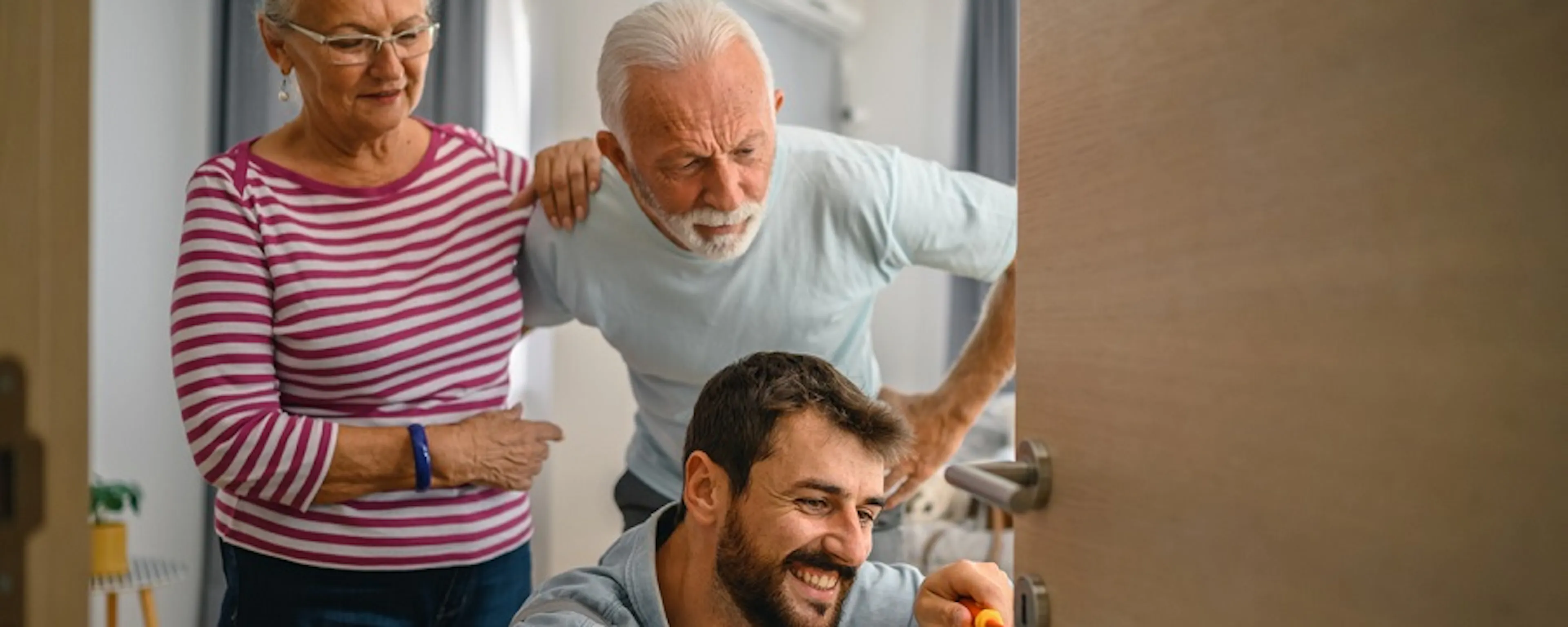 Technicien souriant réparant une porte chez un couple de seniors