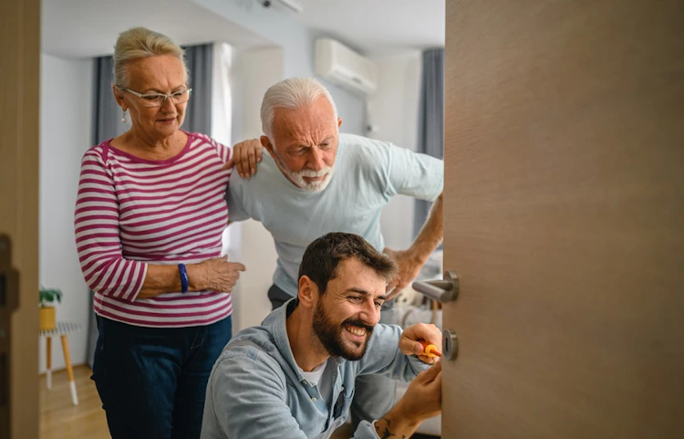 Technicien souriant réparant une porte chez un couple de seniors